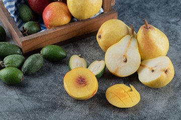 Green feijoa, peach and pears in a wooden tray and on the grey marble