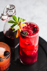 Gin in cocktail garnished with blackberries, lemon slice, and mint.