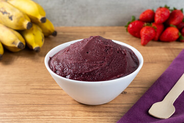 Brazilian frozen açai berry ice cream bowl. with fruits on wooden background. Summer menu front view