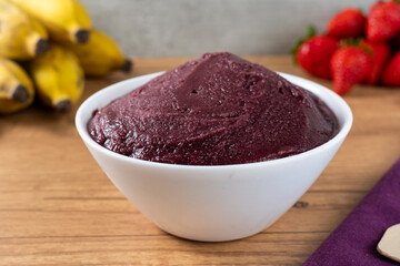 Brazilian frozen açai berry ice cream bowl. with fruits on wooden background. Summer menu front view