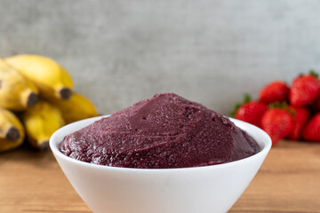 Brazilian frozen açai berry ice cream bowl. with fruits on wooden background. Summer menu front view