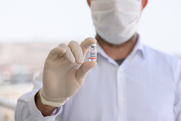 Doctor with white gloves holds bottle with COVID-19 vaccine. Concept of medicine, clinical trial and treatment due to SARS-CoV-2 coronavirus. Blur concept