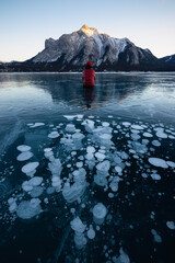 An adventurer poses in front of a group of frozen methane ice bubbles on Lake Abraham at sunset in...