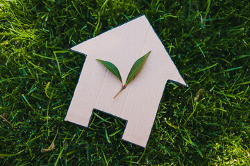 green home and eco-friendly construction, house icon on green grass lawn under the sun with two leaves on top