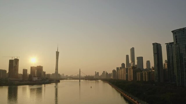Fly over Pearl river with Canton Tower and CDB office buildings district in far distance at beautiful golden sunset. Guangzhou, Guangdong, China.