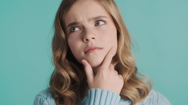 Close up pensive blond teenager girl keeping hand on chin thinking about something isolated on blue background. Face expression