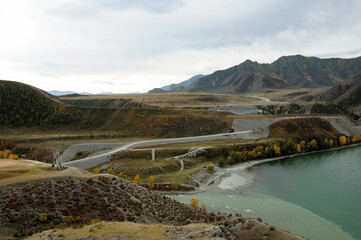 The confluence of two turquoise rivers surrounded by mountains and hills with traces of cars.