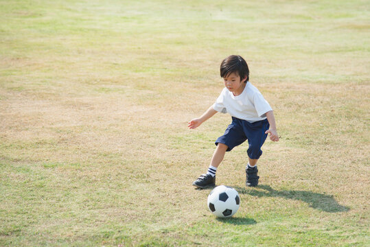 Asian Boy Kicking Football On The Field