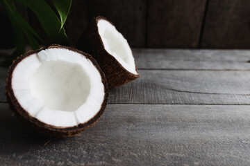 Broken coconuts on gray wooden background with palm leaf. White coconut pulp