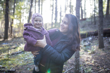 Happy woman holding her adorable baby in the forest