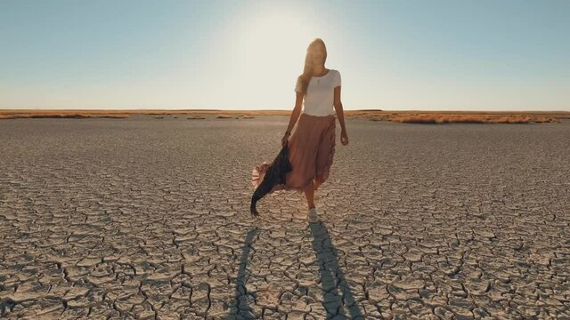 woman walking on the cracked soil.  model walking  on cracked ground of dried lake - ecological disaster concept 4k. golden hour.