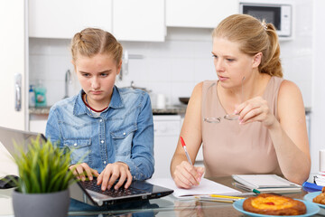 Obraz na płótnie Canvas Attractive woman helping her teenage daughter to do her homework in kitchen