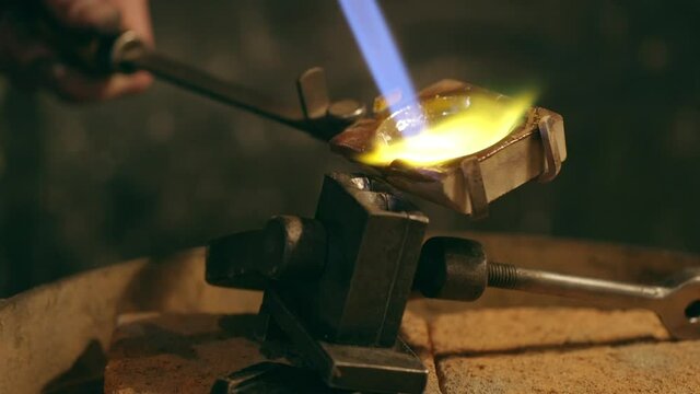 Traditional goldsmith pouring molted metal in mold with goldsmith tools.