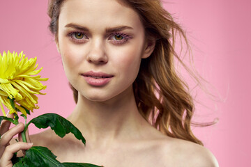 Fototapeta premium Beautiful girl with a yellow flower on a pink background nude shoulders makeup