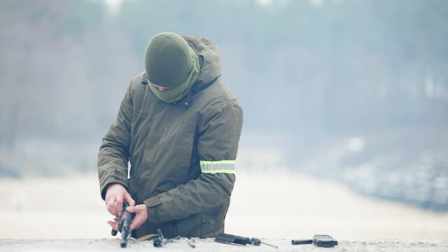 Professional concentrated Caucasian soldier disassembling rifled gun and putting weapon down. Portrait of male recruit training outdoors on polygon. Military concept.