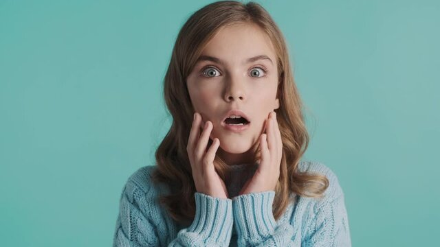 Attractive blond teenager girl looking surprised over blue background. Wow face expression. I can not belive emotion