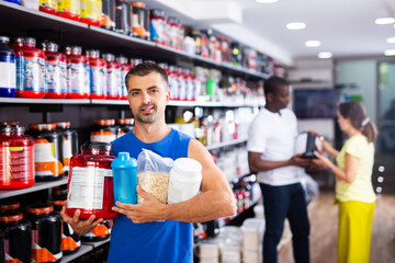 Confident athletic man holding plastic jars of sports food supplements bought in modern shop