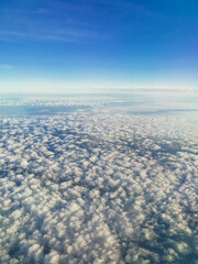 A beautiful view from an airplane on white voluminous fluffy clouds against the background of a bright blue sky, city skyscrapers below, top view, vertical frame