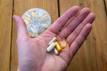 Handful of pills with pill container in background on wooden table