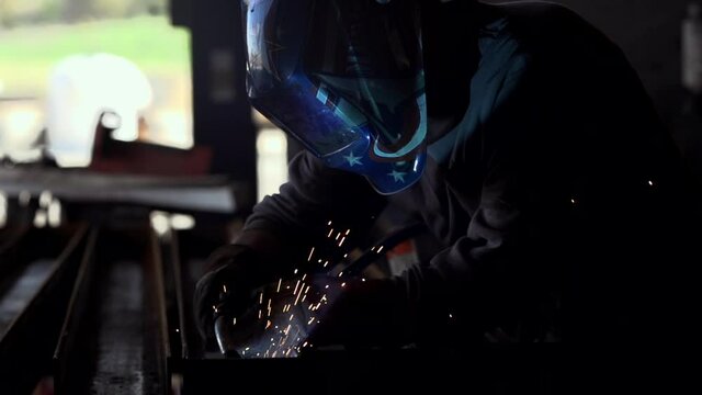 Welder works on a steel beam inside an industrial warehouse with sparks flying. Stock Video