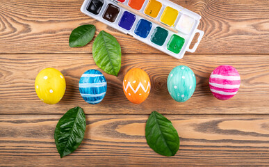Cute Easter eggs decorated handmade with paint and brush on a wooden background with green leaves and young branches