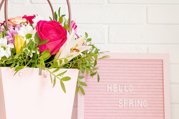 Hello Spring - text on pink felt letter board with blooming flowers and green leaves on whitebrick wall background. Springtime concept. Interior design