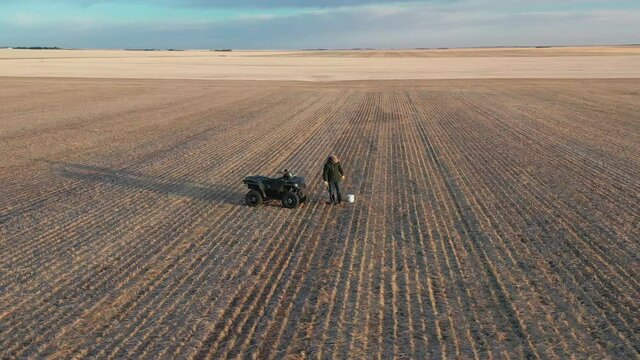Farmer with quad in farm field sampling soil for testing, aerial circling shot