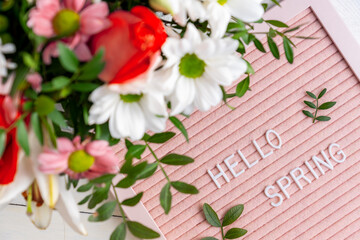 Text Hello Spring on pink letter board and bouquet of colored flowers. Concept Springtime mood and happiness.