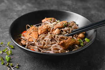 Plate with tasty soba noodles and meat on dark background