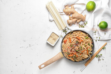 Frying pan with noodles and meat on light background