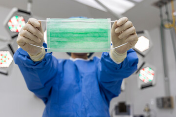 Surgical mask inside modern operating room in hospital.Docto in blue surgical gown suit on background.Shallow DOF and blurred background. Mask to protect form airborne disease.