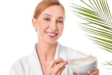 Beautiful young woman with bowl of facial cream and tropical leaf on white background