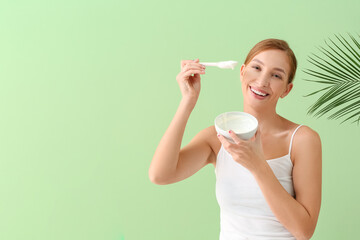 Beautiful young woman with facial cream and tropical leaf on color background