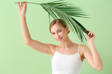 Beautiful young woman with tropical leaf on color background