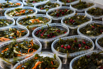 Different fish and chuka wakame laminaria seaweed salad in plastic bowles. Concept of healthy food production or delivery food