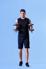 Sporty young man training with dumbbells on color background