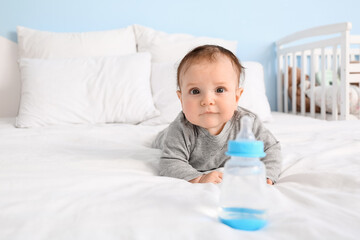 Cute baby boy with bottle of water at home