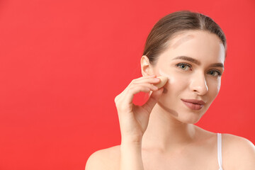 Beautiful young woman applying contouring makeup against color background