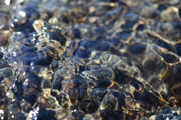 beautiful ripples on river flow over colorful stones in summer sunshine