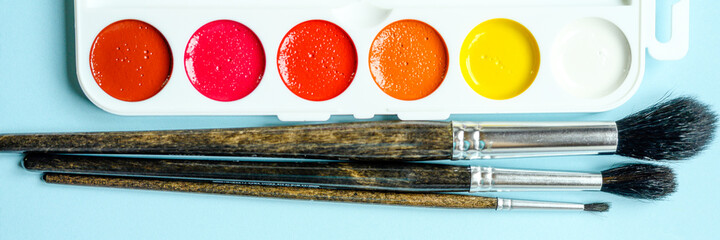 Box of watercolor paints and brushes for drawing on blue background. banner