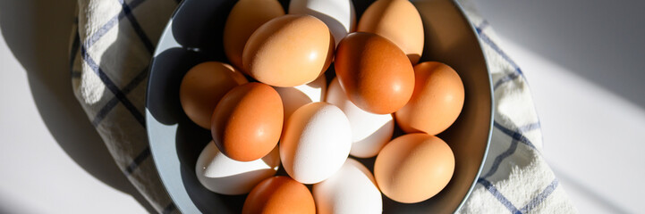 chicken eggs white and brown color in a gray plate on a checked kitchen towel on a white table. concept farm products and natural nutrition. hard sunlight and shadows. banner