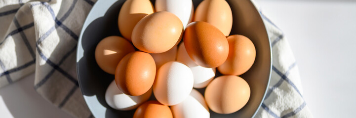 chicken eggs white and brown color in a gray plate on a checked kitchen towel on a white table....