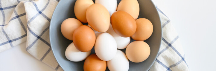 chicken eggs white and brown color in a gray plate on a checked kitchen towel on a white table. concept farm products and natural nutrition. banner