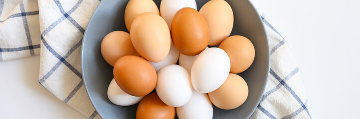 chicken eggs white and brown color in a gray plate on a checked kitchen towel on a white table. concept farm products and natural nutrition. banner