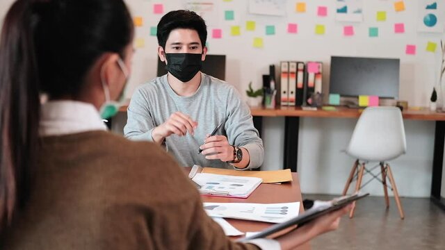 Company workers, man and woman, sit for meetings, wear masks and maintain social distance. Prevent the spread of the corona virus. There is alcohol gel to wash your hands on the conference table.