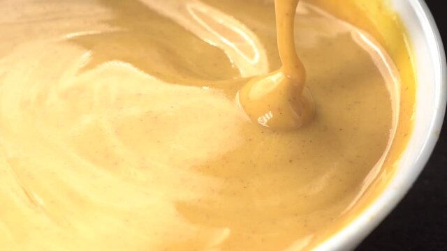 Slow motion closeup view of spoon stirring sweet delicious looking custard cream. Sauce dripping from spoon into ceramic glass.