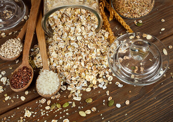 Glass jar of oat flakes with wheat ears, spoons of brown and white rice, pearl barley with chia and...