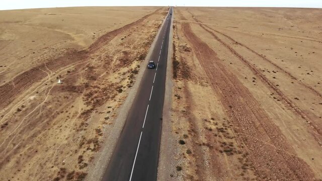 An Overhead View Of A Car Driving Along An Empty Highway On A Sunny Day. The Drone Follows The Vehicle Along A Narrow Asphalt Road. Car Driving Through The Desert