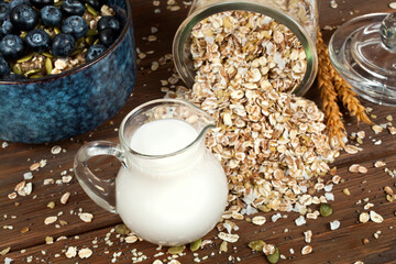 Oatmeal porridge with blueberries in a blue ceramic bowl, oat flakes and jug of vegetable almond milk on a wooden background. Healthy eating concept.