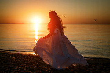 Fototapeta na wymiar Young free woman running in white dress near the sea at sunset